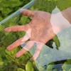 A hand is shown through a transparent PVC tarp, with green foliage in the background. Náhled obrázku produktu