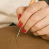 A close-up shot of a hand with red nail polish using a sculpting tool to carve into a brown clay surface. Produktbild-Vorschau