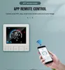 A smart thermostat is shown on a wall, with a hand holding a smartphone displaying the thermostat's app interface. Voir les images du produit