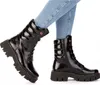 A pair of black patent leather boots worn by a person in blue jeans. Anteprima dell’immagine prodotto