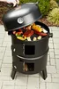 A person's hand is shown opening the lid of a black charcoal grill filled with food. Náhled obrázku produktu