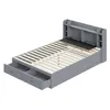 A grey wooden bed frame with drawers and a headboard with shelves, shown from a diagonal angle against a white background. Produktbild-Vorschau