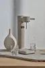 A carbonator and vase are displayed on a textured surface with two glasses. Produktbild-Vorschau