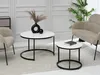 Two round coffee tables with white tops and black metal bases are placed on a rug in a living room setting. One table has a black vase with dried flowers and a black sphere on it, while the other has a book. Náhľad obrázku produktu