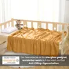 A yellow fleece blanket is draped over a child's bed, with a teddy bear and pillow on the bed. Produktbild-Vorschau
