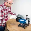 A man in a red and white checkered shirt and safety glasses is using a bench grinder to sharpen a tool. Náhľad obrázku produktu