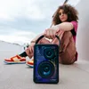 A person is sitting on the ground holding a portable speaker. The person is wearing casual clothing and sneakers. The background is an outdoor urban setting with a cloudy sky. Produktbild-Vorschau