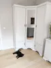 A black cat lies on a light-colored wooden floor in front of a white corner wardrobe with mirrored doors. Náhľad obrázku produktu