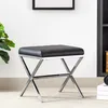 A black upholstered stool with a chrome X-shaped base sits on a carpeted floor in front of a white wall. Náhled obrázku produktu