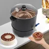 A commercial wax melting pot with a glass lid, a tap, and a bowl of chocolate being held under the tap. A cake is also visible on the left. Náhled obrázku produktu
