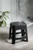 A black plastic stool is placed on a tiled floor in a bathroom, next to a shower enclosure and a potted plant. Produktbild-Vorschau