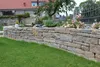 A garden scene with a stone wall and plants. Produktbild-Vorschau