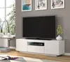 A white TV stand with a television on top, placed in a living room setting with artwork on the wall and a window in the background. Náhled obrázku produktu