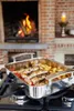 A roasting pan filled with food is placed on a stovetop in front of a fireplace. Produktbild-Vorschau