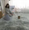 A woman is sitting on a fluffy gray rug in a room with soft lighting. Náhled obrázku produktu