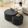 A woman is sitting on the floor next to two round ottomans, using a laptop on the larger one. A bowl of fruit is on the smaller ottoman. Produktbild-Vorschau