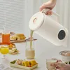 A person is pouring a drink from a soy milk maker into a glass, with breakfast items on the table. Podgląd zdjęcia produktu