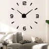 A large wall clock is mounted on a white wall above a sofa in a living room. Produktbild-Vorschau