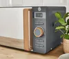 A modern gray microwave with a wooden handle and trim sits on a wooden countertop next to a potted plant. Náhled obrázku produktu