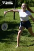 A young woman playing badminton in a grassy park. Produktbild-Vorschau