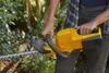 A person is holding a yellow hedge trimmer in a garden setting. Produktbild-Vorschau