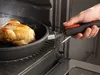 A hand is shown removing a cooked chicken from an oven in a pan. Anteprima dell’immagine prodotto