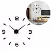A close-up of a large, modern wall clock with black numbers and hands on a white background. A smaller inset image shows the clock installed on a living room wall. Produktbild-Vorschau