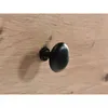 A close-up of a black drawer knob on a wooden surface. Produktbild-Vorschau