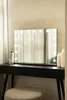 A vanity mirror with LED lights sits on a black dressing table, with a stool in front. Produktbild-Vorschau
