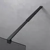 A close-up view of a black shower support arm attached to a glass shower panel, set against a textured gray wall. Anteprima dell’immagine prodotto