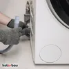 A person wearing gloves is connecting a washing machine drain hose to the back of a washing machine. Produktbild-Vorschau
