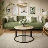 A living room scene featuring a green sofa, a round wooden coffee table, and wall art. Produktbild-Vorschau