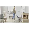 A woman is vacuuming a living room with a cordless vacuum cleaner. Voir les images du produit