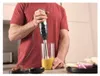 A person is using an immersion blender to blend a yellow mixture in a glass. Produktbild-Vorschau