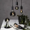 A collection of decorative LED light bulbs with a smoky glass finish, some hanging and some on a table, with a potted plant in the background. Podgląd zdjęcia produktu