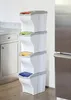 A stack of four white trash bins with colored lids, placed in a kitchen setting next to a refrigerator and cabinets. Náhľad obrázku produktu