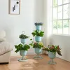 A living room with a couch, a window, and several potted plants on stands. Produktbild-Vorschau