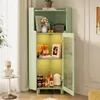 A green cabinet with glass doors, displaying various items on its shelves, including books, bottles, and a kettle. The cabinet is placed in a room with a window and curtains. Produktbild-Vorschau