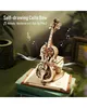 A wooden 3D model of a cello with a bow, placed on top of books, with musical notes and light effects around it. Náhľad obrázku produktu