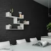 A modern white wall shelf unit is mounted on a black brick wall, displaying various decorative items and kitchenware. In the foreground, a white dining table with chairs is visible. Anteprima dell’immagine prodotto