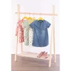 A wooden children's clothes rack with several dresses hanging on it and a pair of pink boots on the shelf below. Produktbild-Vorschau