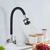 A kitchen faucet with a flexible black hose and silver head is mounted on a white marble-patterned wall. Several white ceramic containers with wooden lids and a bunch of red grapes are on the counter below. Náhľad obrázku produktu