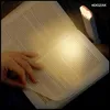 A hand is turning the page of an open book, illuminated by a small LED reading light clipped to the top of the book. Náhľad obrázku produktu