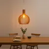 A wooden pendant light hangs over a dining table set with plates and a vase of greenery. Voir les images du produit