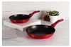 Two red frying pans are displayed on a table with a white block and a small plant in the background. Podgląd zdjęcia produktu