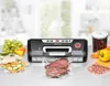 A vacuum sealer machine is shown on a countertop with various foods, including meat, vegetables, and fruits, either packaged or waiting to be packaged. Produktbild-Vorschau