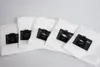 A group of five white vacuum cleaner bags with black plastic connectors are laid out on a light gray background. Produktbild-Vorschau