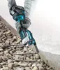 A person wearing gloves is using a Makita cordless multi-tool to cut into concrete, with rebar visible underneath. Produktbild-Vorschau