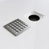 A square shower drain grate and its housing are shown on a textured white surface. Anteprima dell’immagine prodotto