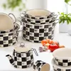 A collection of cookware with a black and white checkerboard pattern, including pots, a teapot, and storage containers, arranged on a white surface with some vegetables in the background. Produktbild-Vorschau